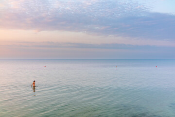 Fototapeta premium Rear view of a woman in brown swimwear going into the sea on the beach at sunrise