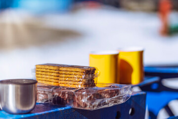 two yellow mugs with a hot drink and cookies with marshmallows on a metal structure on a winter day