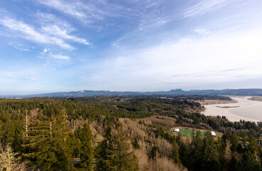Wide angle landscape view of distant ball field and mountain range with fir trees and bright blue sky in the Pacific Northwest.