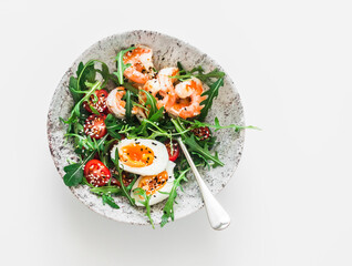 Breakfast, snack  bowl - arugula, cherry tomatoes salad with boiled egg and fried shrimp on a light background, top view