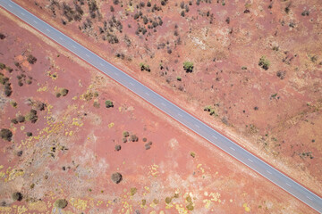 Looking down at the diagonal asphalt road with the red Australian dirt and bushes on both sides of the road.