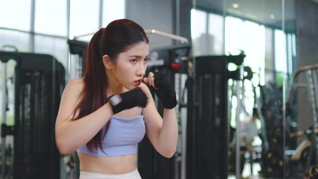 Serious asian athletic woman punching the air with her fists training warm-up before boxing workout at gym club. Sports. Activity. Motivation. Confidence, working out on boxing moves.