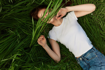 happy woman lies in tall grass covering her face with leaves