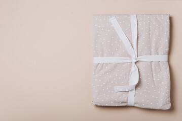 Stack of clean bed sheets with bow for present or gift on beige background. Top view. Copy space
