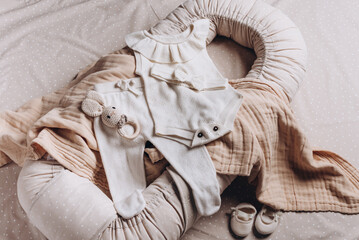 Baby clothes, accessories, toys set on neural background. Fashion newborn essentials. Top view. Girl romper, leggings, head bow, pacifier holder, bib, teether, crocketed toy over beige cocoon, nest