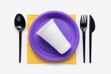 On a yellow napkin is a purple plate and cutlery. Plastic recycling. Studio shot, top view.