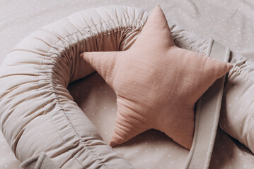Soft star pillow toy on beige cocoon, baby nest for newborn over cribs in nursery. Childhood...