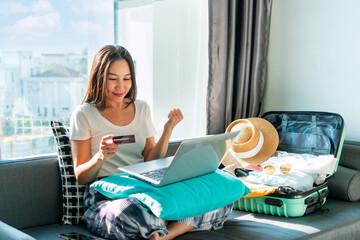 Happy young Asian woman using credit card booking flight tickets and hotel at home. Planning a trip and online booking, cashless society, technology and lifestyle, Summer vacation concept. Free space