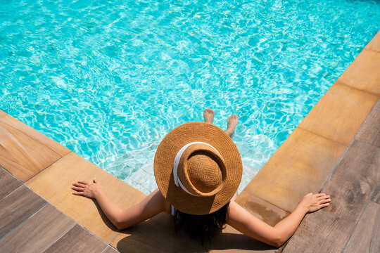 Top view of woman wear a hat sitting and relaxing in swimming pool, swimming pool scenery on background. Summer holidays, vacation, travel concept. Copy space