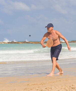 A handsome mature man hits a ball while playing matkot on the beach