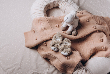 Obraz premium Soft sheep toy on beige cocoon, baby nest for newborn over cribs in nursery. Childhood concept. Eco-friendly safe goods and toys for children. Light kid's room interior. Time for sleep