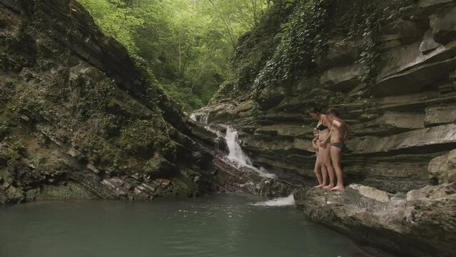 Woman with children by pond in forest. Creative. Natural waterfall with pond and bathing tourists. Family with children swim in natural pond with waterfall in forest