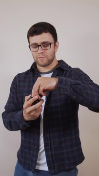 Vertical video: Cheerful white man, wearing blue and white clothes, smelling and putting perfume on his neck in a professional and sophisticated way, on a beige background.