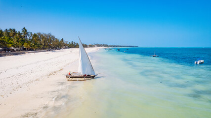 Obraz premium Take in the breathtaking beauty of Zanzibar's tropical coastline from above, as fishing boats dot the sandy beach at sunrise. The view from the top highlights a clear blue sea, green palm trees, 