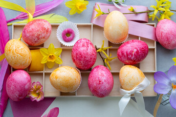 In einem frühlingshaft dekorierten Setzkasten liegen gelbe und rosa gefärbte Ostereier