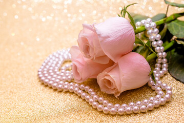 Pink rose and pearl necklace on a shiny gold background
