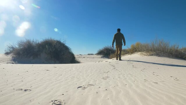 Adult black male walking hiking away on white sands national park sand dunes landscape with mountains in New Mexico, USA