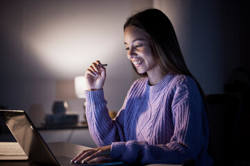 Woman, happy or laptop reading in night studying, education or homework research in living room on...