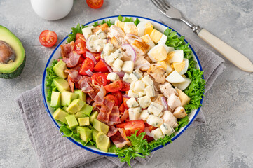 Tradition Cobb salad with fried chicken, avocado, fresh tomatoes, eggs, bacon and cheese on a plate. selective focus