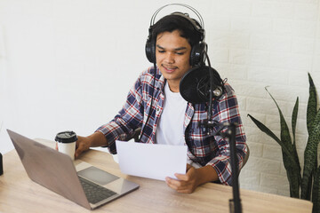 Young asian man radio host reading news from paper while sharing information at podcast studio. - Powered by Adobe
