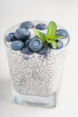 Homemade organic sweet pudding dessert made of chia seeds soaked in healthy plant based milk decorated with topping of ripe blueberries and fresh mint leaf served in glass on white wooden background