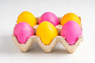 Bright dyed and boiled decorated homemade easter eggs of yellow and pink colours served in carton tray or container prepared as symbol for traditional celebration on white wooden background