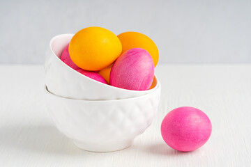 Colorful dyed and boiled decorated homemade easter eggs of yellow and pink colours served in two ceramic bowls prepared as symbol for traditional celebration on white wooden table at kitchen