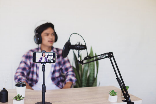 Video screen recording of young happy confident male student in front of smartphone camera making video content sharing studying tips against blurred content creator background. 
