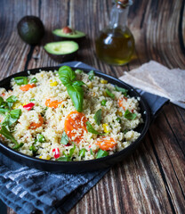 Delicious homemade vegetarian couscous with tomatoes, carrots, zucchini, yellow bell pepper and fresh basil. on a dark rustic wooden kitchen table