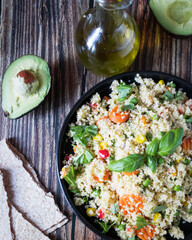 Delicious homemade vegetarian couscous with tomatoes, carrots, zucchini, yellow bell pepper and fresh basil. on a dark rustic wooden kitchen table