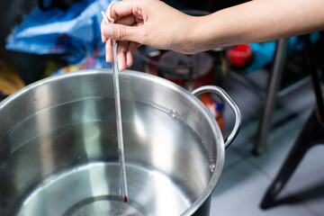 A hand holding a thermometer to measure the temperature of the water being boiled.