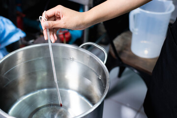 A hand holding a thermometer to measure the temperature of the water being boiled.