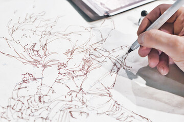 Close-up shot of the hand of a comic book artist painting a manga cartoon character in ink line...