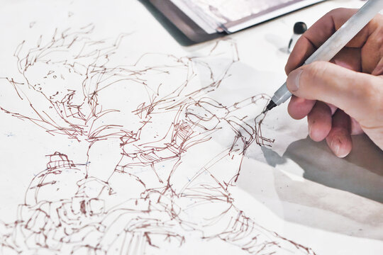 Close-up shot of the hand of a comic book artist painting a manga cartoon character in ink line drawing