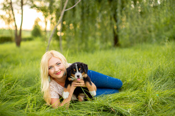 A beautiful girl with a dog sits in the park on the grass. Love to the animals. Home pet on a walk. Animal protection. Bernese mountain dog puppy.