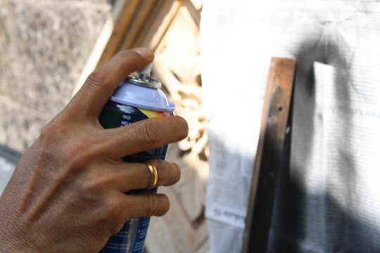 A worker painting steel angle or angle iron in black with spray paint or aerosol paint to create shelves