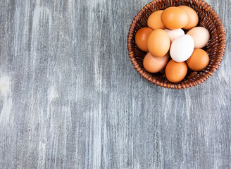 Fresh chicken eggs in a wicker bowl on a gray wooden textured background