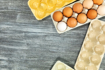 A dozen fresh chicken eggs in a cardboard tray and empty cardboard egg trays on a gray wooden textured background