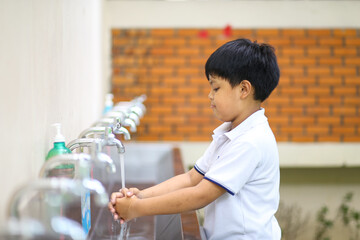 An Asian school boy washing his hand at an outdoor faucet sink and water tab in a school. 