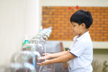 An Asian school boy washing his hand at an outdoor faucet sink and water tab in a school. 