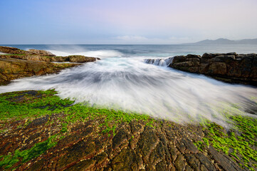 White waves wash over mossy brown rocks. Explore breathtaking coastal landscape. Clear Waters, and Stunning Views of the Pacific Ocean in New Taipei City.
