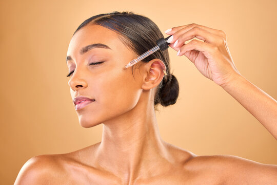 Face, skincare serum and woman with eyes closed in studio isolated on brown background. Dermatology, cosmetics and Indian female model with hyaluronic acid, retinol or essential oil for healthy skin.