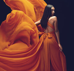Fashion, portrait and woman in orange dress in studio isolated on a black background. Beauty,...