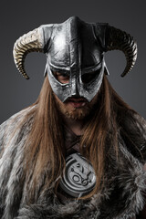 Studio shot of fierce nordic warrior with long hairs dressed in fur and horned helmet.