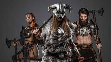 Portrait of three scandinavian warriors from past with fur against grey background.