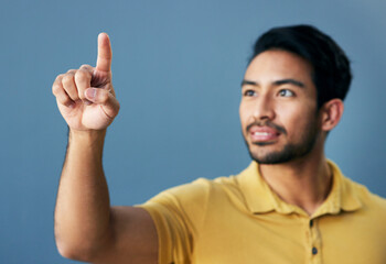 Finger, pointing and asian man with invisible hologram in studio with mockup against blue background. Interface, hand and creative male entrepreneur with advertising, marketing or idea while isolated