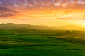 countryside sunset in green hills of spring fields with old castle farm and mountains on background of evening landscape