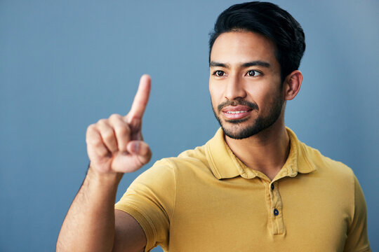 Pointing, finger and asian man with invisible hologram in studio with mockup against blue background. Interface, hand and creative male entrepreneur with advertising, marketing or idea while isolated