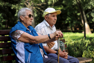 Elderly couple sitting on a bench in spring or summer park. Old man and woman outdoors, life in...