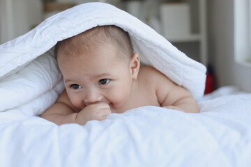 Cute baby boy crawling on the bed while playing with hands, body covered by the blanket. Happy moments.